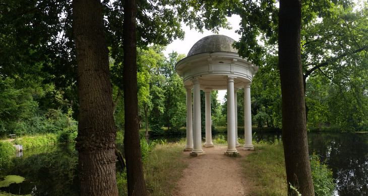 Kleiner Säulentempel im Schlosspark Lützschena. Er steht auf einer kleinen Halbinsel in einem Teich mit vielen Bäumen drum herum.