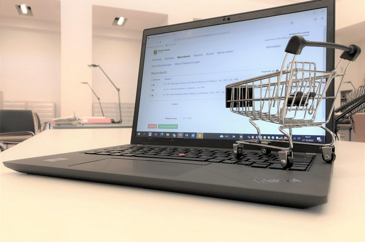 Miniatureinkaufswagen auf der Tastertur eines Laptops der die Internetseite des Stadtarchivs mit der Bestellfunktion zeigt.