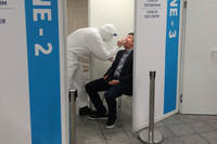 Ein Mensch in Schutzanzug und mit Maske und Gesichtsvisier nimmt eine Rachenprobe für einen Coronatest von einem Mann.