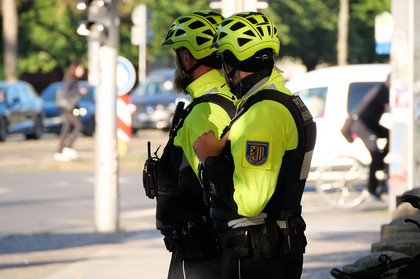 Zwei Mitarbeiter der Polizeibehörde in Uniform blicken auf eine vielbefahrene Kreuzung.