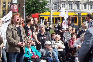 Eine Menschengruppe, darunter einige Rollstuhlfahrer, auf dem Richard-Wagner-Platz. Im Hintergrund sieht man eine Straßenbahn.