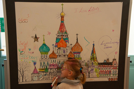 Ein Mädchen malt mit bunten Stiften ein großes Plakat an, welches die Basilius-Kathedrale zeigt.