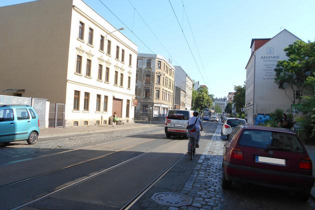 Ansicht der Dieskaustraße mit fahrenden und parkenden Autos und einem Radfahrer. In der Mitte liegen Straßenbahngleise, daneben ist die Straße gepflastert.