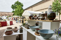 Mehrere Keramikschüsseln und -vasen stehen auf einem Stand in einem Innenhof. 