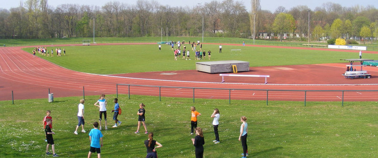 Sportler stehen auf einer Wiese im Kreis und machen Übungen. Im Hintergrund eine Rennbahn i, Leichtathletikstadion Nordanlage Sportforum