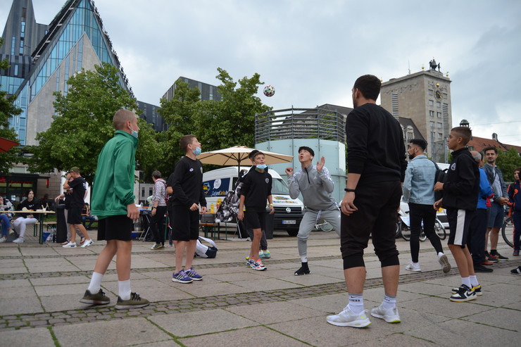Auf dem Leipziger Augustusplatz steht ein Kreis aus Jugendlichen, die Fußball spielen