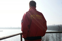 Rettungsschwimmer in Berufskleidung (Schriftzug DLRG) blickt nachdenklich auf einen See.
