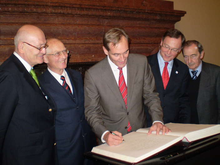 Bürgermeister Burkhard Jung steht neben anderen Männern und trägt sich in das Goldene Buch der Stadt Hannover ein
