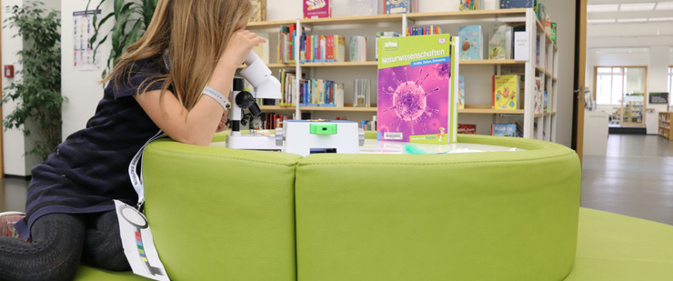 Ein Mädchen schaut in der Kinderbibliothek durch ein Mikroskop