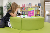 A girl in the kids library, looking trough a microscope.