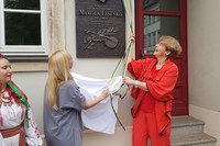 Links im Bild die Leiterin des Kulturamts der Stadt Kyjiw (eine blonde Dame im blauen Kleid), rechts Frau Dr. Goldfuß von der Stadt Leipzig (in roter Kleidung). Beide haben eben die Gedenkplatte enthüllt und halten noch das Tuch in Händen. Sie schauen hoch zur Gedenktafel an der Hauswand.