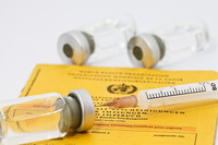 Spritze auf gelbem Impfpass liegend.