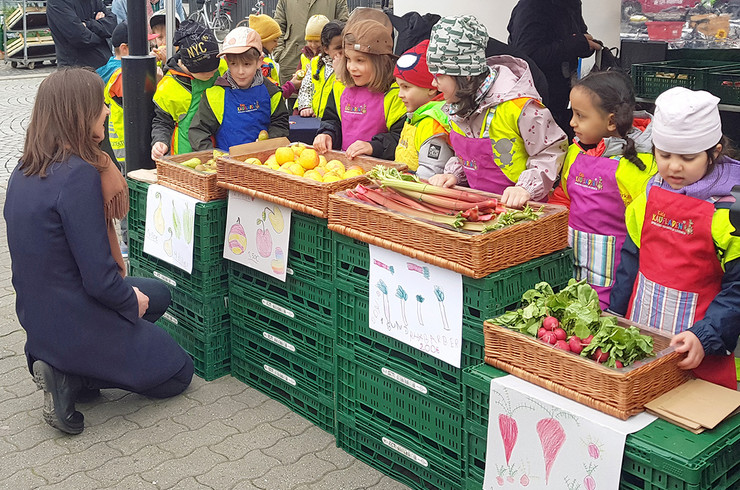 Viele Kinder an einem Marktstand als Verkäufer. Angeboten wird Gemüse mit selbst gemalten Bilder.