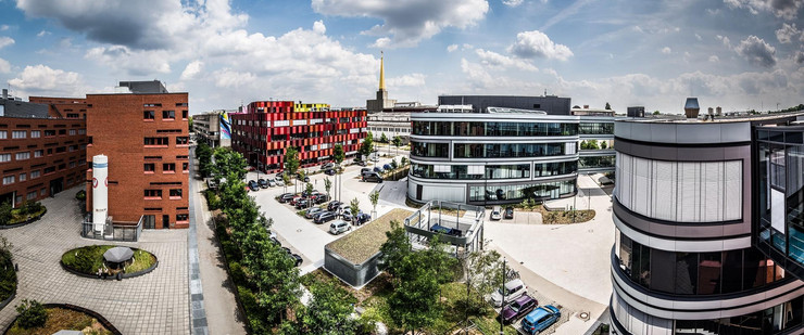 Viele Gebäude auf dem Campus der BioCity in Leipzig. Dazwischen Bäume und parkende Autors und ein Himmel mit einzelnen Wolken.