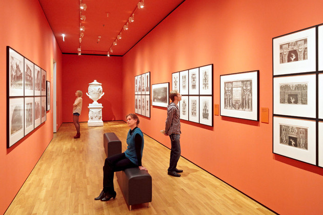Besucher betrachten in einer Ausstellung verschiedene an der Wand hängende Zeichnungen