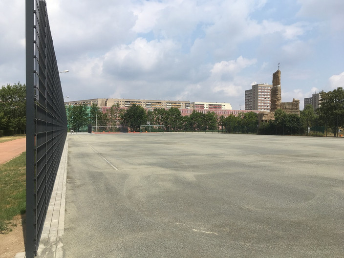 Großspielfeld für Fußball mit grauem Belag und Metallzaun