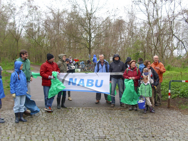 Mitglieder des Naturschutzbundes NABU halten ihr Logo und Mülltüten am Fuße des Fockebergs