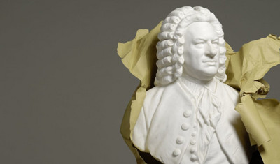 Eine weiße von Johann Sebastian Bach ragt aus zerrissenem Papier