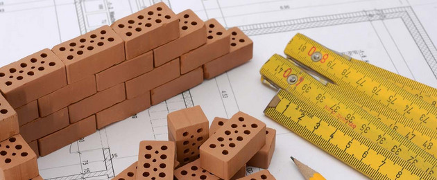 Auf einer Bauzeichnung sind Bausteine, ein Zollstock und ein Stift zu sehen.