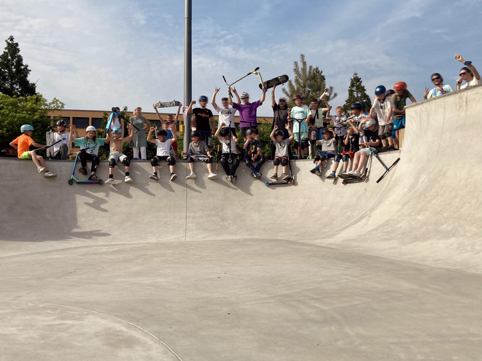 Foto von jungen Skatern, die auf dem Rand der Skateanlage sitzen und stehen und in die Kamera grüßen.