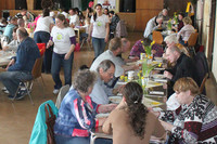 Viele Menschen sitzen ein einem Saal an Tischen und essen.