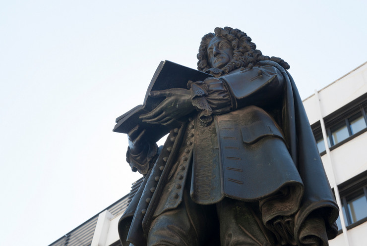 Das Foto zeigt das Leibnizdenkmal. Leibniz hält ein aufgeschlagenes Buch in den Händen.