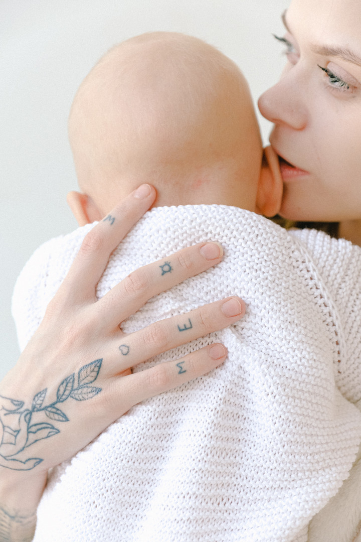 Eine Frau hält ein Baby auf dem Arm. Ihr Mund ist am Ohr des Babys