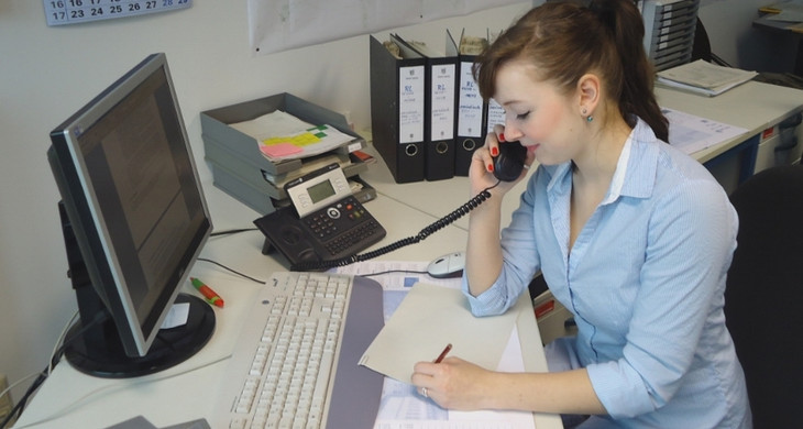 Eine Mitarbeiterin sitzt an einem Büroarbeitsplatz vor einem Computer und telefoniert.