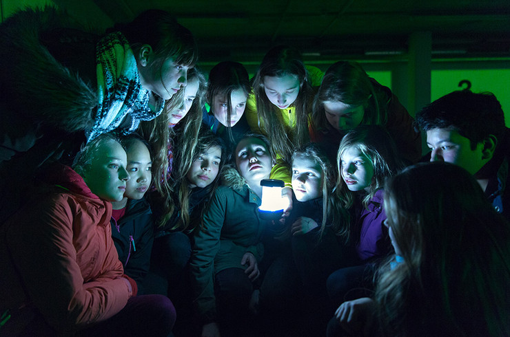 Elf Kinder stehen in dunklem Raum um eine Taschenlampe herum