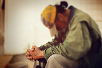 Obdachloser Mensch sitzt mit nach unten geneigten Kopf