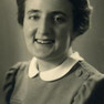 Porträt einer lachenden, jungen Frau mit langem, um den Kopf gelegtem Haar, dunkelm Kleid mit weißem Bubikragen