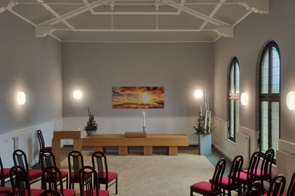 Raum für Trauerfeiern mit Stühlen, einem Rednerpult und Pflanzendekorationen