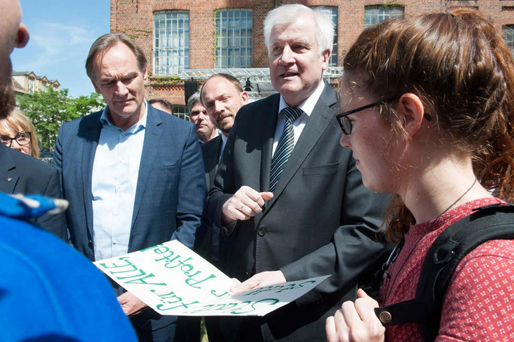 Horst Seehofer und Burkhard Jung umringt von Menschen. Herr Seehofer hält ein handschriftliches Plakat in der Hand.