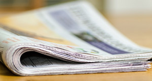 Auf einem braunen Tisch liegt eine zusammengefaltete Zeitung, die nach hinten verschwommen dargestellt wird.