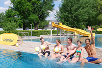 Junge Menschen sitzen am Rand des Schwimmbeckens im Schreberbad und testen das kühle Wasser.