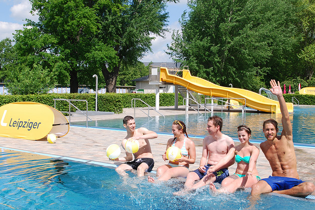 Junge Menschen sitzen am Rand des Schwimmbeckens im Schreberbad und testen das kühle Wasser.