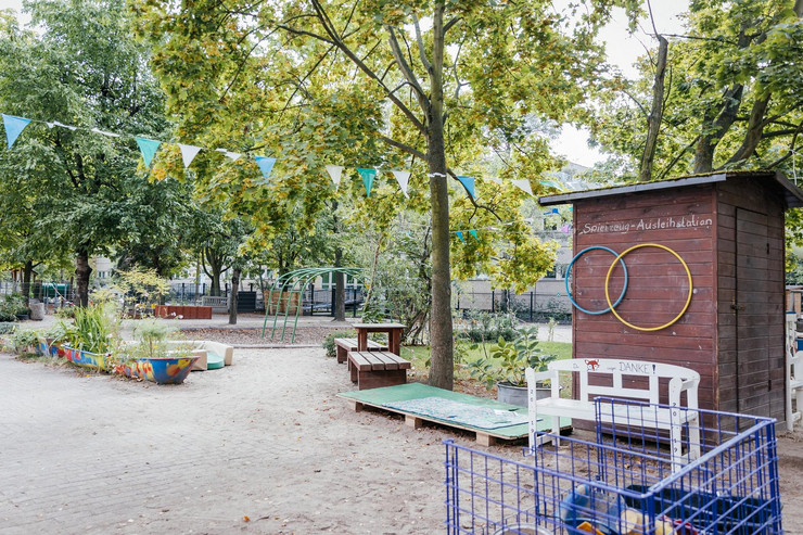 Garten einer Kindertagesstätte mit Spielgeräten, Bänken und Pflanzen.