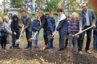Mehrere Kinder und Erwachsene graben gemeinsam mit Schaufeln Erde um.