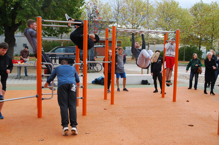 Mehrere Jugendliche machen verschiedene Sportübungen an einem Stangen-Fitnessgerät im Freien. 