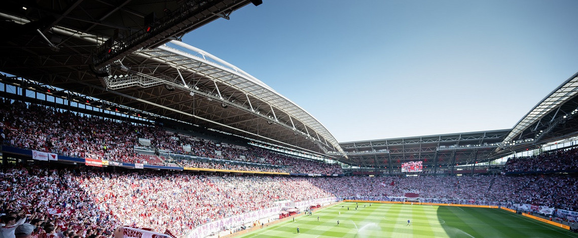 Die ausverkaufte Red Bull Arena, fotografiert aus dem RB-Fanblock. Im Vordergrund halten Fans ihre Schals nach oben.