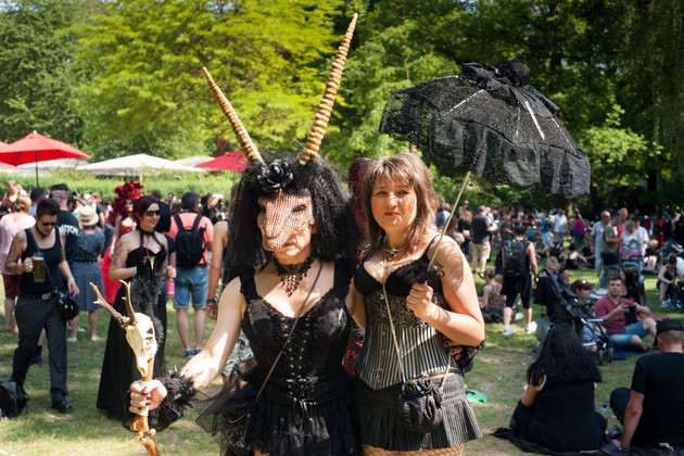 Zwei Frauen in szenetypischer dunkler Kleidung beim Wave Gotik Treffen in einem Park mit vielen Menschen.