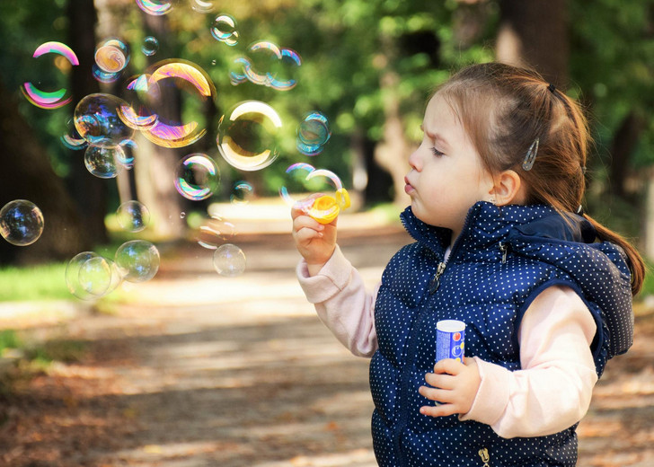 Kleinkind steht auf einem Wanderweg und pustet Seifenblasen in die Luft.