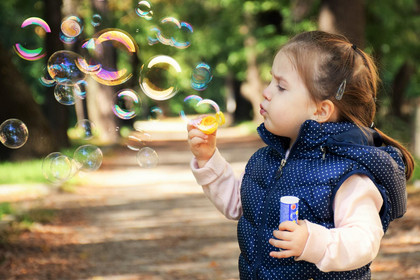 Kleinkind steht auf einem Wanderweg und pustet Seifenblasen in die Luft.