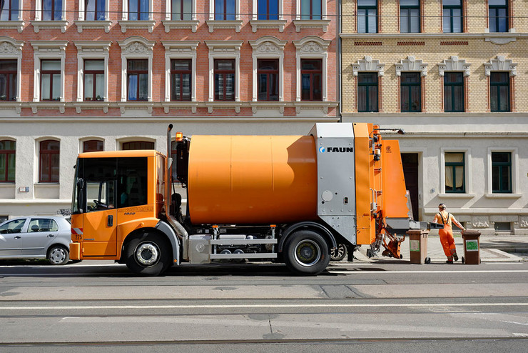 Ein Abfallsammelfahrzeug der Stadtreinigung steht an einer Straße. Ein Mitarbeiter zieht zwei Biotonnen zum Gehweg.