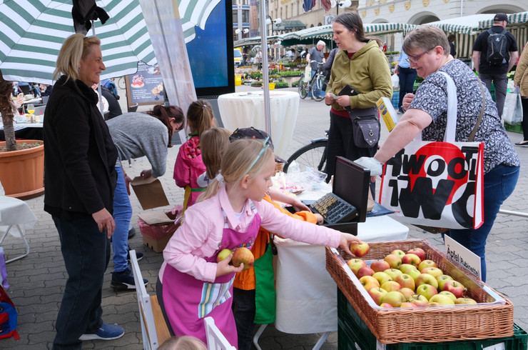 Vier Kinder verkaufen Obst an zwei Frauen an einem Marktstand