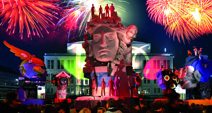 Visualisierung mehrerer überlebensgroßer Skulpturen zum Stadtfestspiel auf dem Augustusplatz. Eine Menschenmenge schaut zu. Ein Feuerwerk ist am Himmerl.