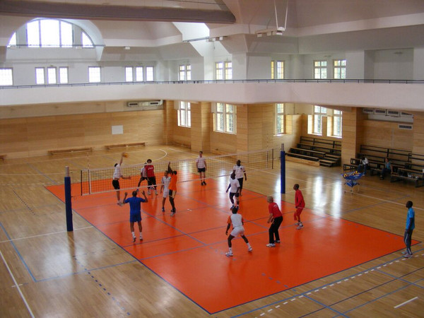 Zwei Mannschaften spielen Volleyball gegeneinander in einer Sporthalle.