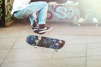 Beine eines Mannes, die sich gerade von einem Skateboard abstoßen. das Skatboard fliegt und dreht sich.