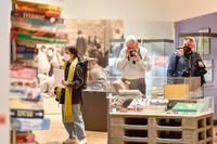 Besucher in den Ausstellungsräumen zwischen Ausstellungsobjekten, unter anderem gestapelte Spielkartons