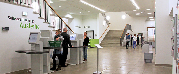 Foyer des Erdgeschosses der Leipziger Stadtbibliothek, Kunden stehen an Selbstverbuchungs-Automaten und entleihen Medien